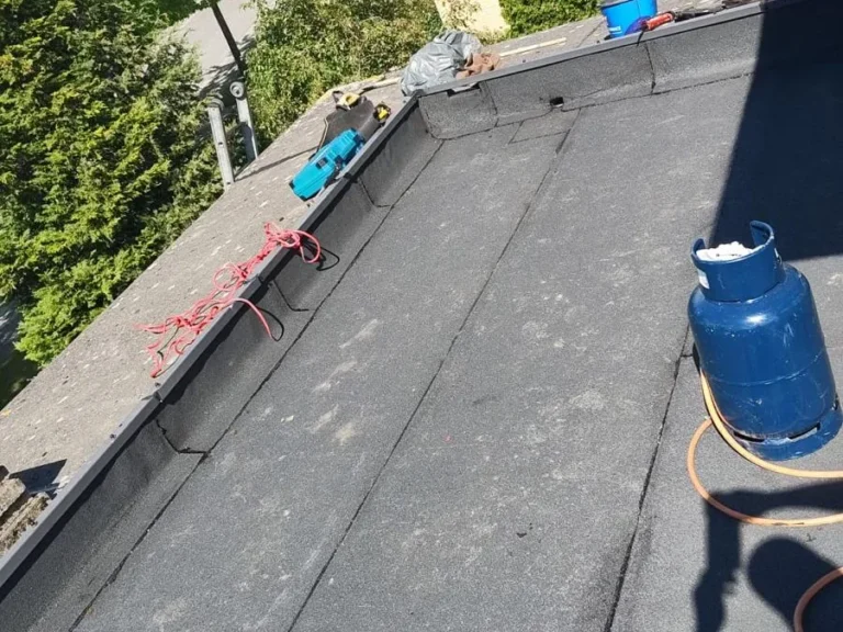 Nieuwe bitumen dakbedekking wordt langs de dakrand gebrand op een plat dak in Lelystad